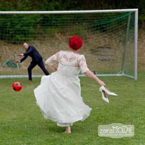 Fussballspiel zwischen Braut und Bräutigam mit einem roten Ball, sie schießt und er steht im Tor