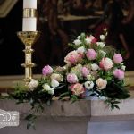 Altargesteck mit rosa und gelben Rosen und Ständer der Kerzen auf dem Altar