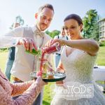 Sandzeremonie: Braut und Bräutigam schütten grünen und roten Sand aus zwei verschiedenen Gläsern in ein Glas als Symbol ihrer untrennbaren Einheit